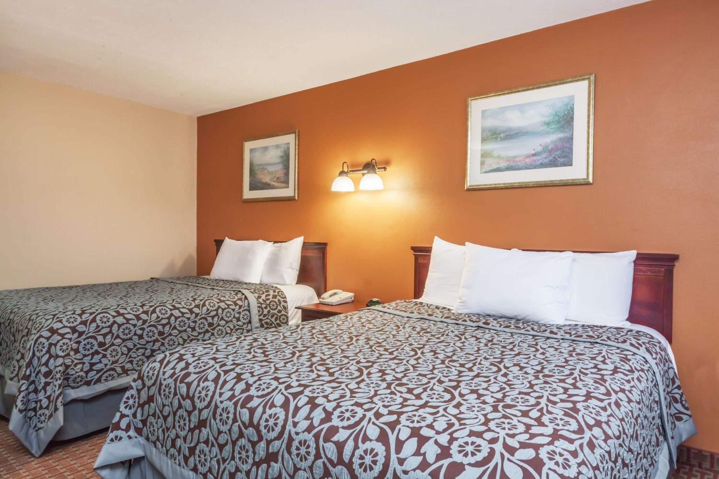 Habitación de hotel con dos camas, una mesita de noche, una lámpara y dos cuadros en la pared.