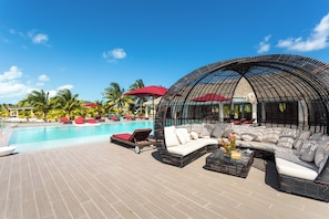 A poolside area with a curved seating area, a pool, and palm trees. - Turtle Island Beach Resort Trademark Collection by Wyndham (San Pedro)