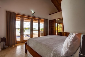 Quarto com uma cama grande, vista para uma piscina e água, e uma porta que dá para o exterior.