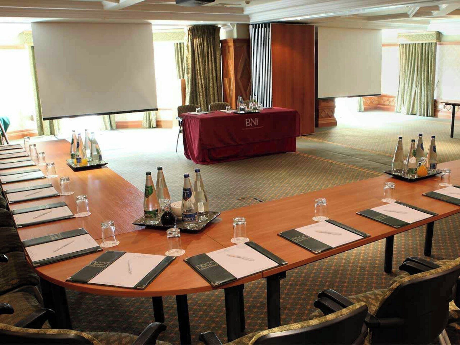 Un salón de conferencias con una larga mesa dispuesta para reuniones, equipado con botellas de agua, vasos y tarjetas de identificación.