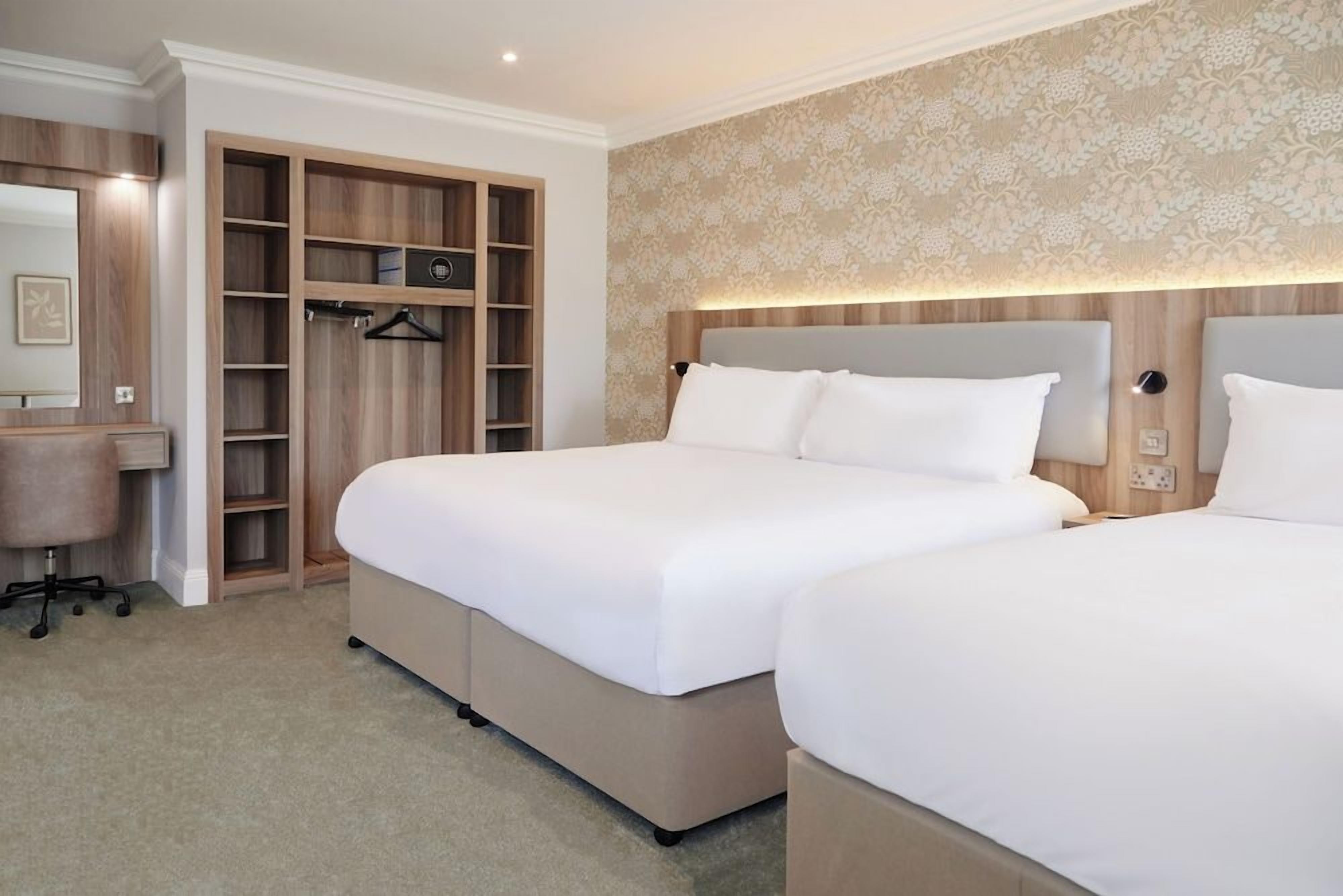 Una habitación de hotel con dos camas, un armario, un escritorio y un espejo.