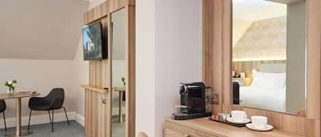Habitación de hotel con un escritorio de madera, televisor, cafetera y espejo que refleja la habitación.