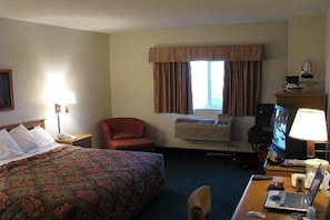 A hotel room with a bed, a desk with a computer, a chair, a lamp, and a window with curtains.