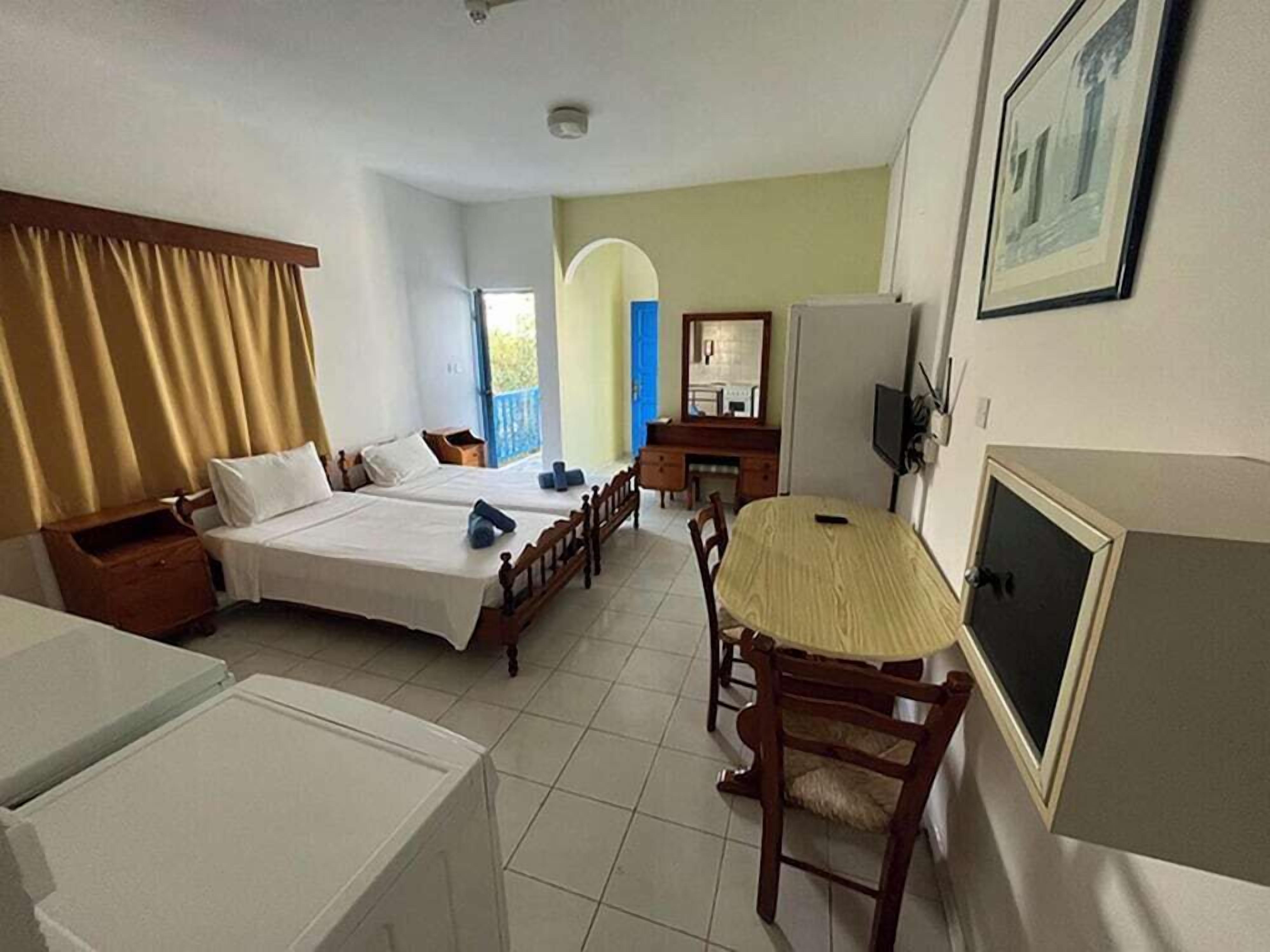 A hotel room with two beds, a dining table, a TV, and a bathroom.