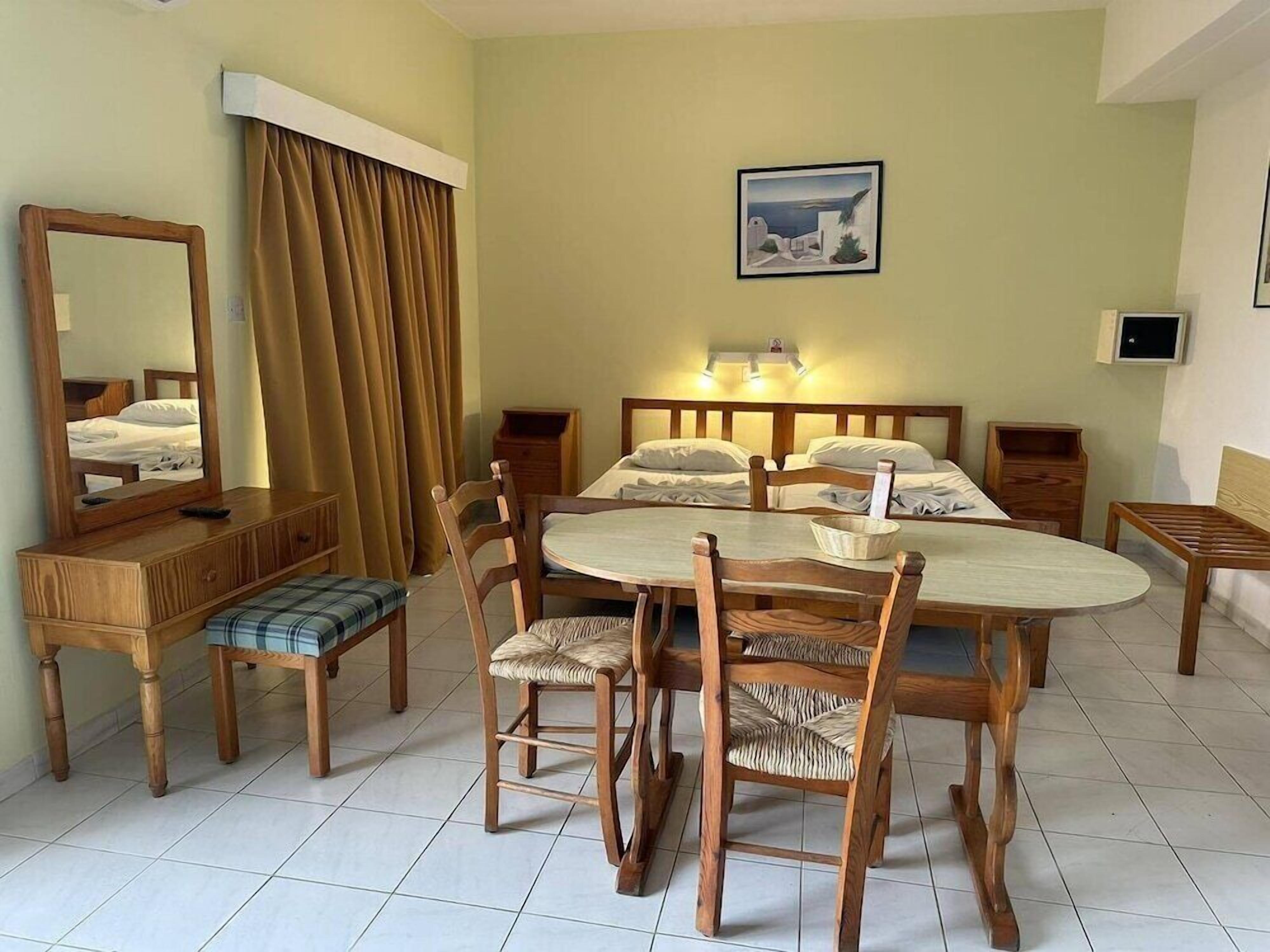 Una habitación de hotel con cama, una mesa de comedor con sillas, un espejo, un televisor y un cuadro en la pared.