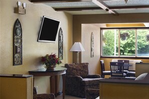 A room with a large window, a flat-screen TV mounted on the wall, a table with a vase of flowers, and a chair. - Super 8 by Wyndham Whitewater WI (Whitewater)