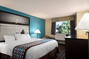 A hotel room with a bed, a desk, a lamp, a window with curtains, and a painting on the wall. - Super 8 by Wyndham Whitewater WI (Whitewater)