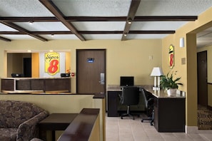 Zona de recepción de un hotel con un mostrador, un sofá, un escritorio con una computadora y un televisor.