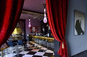 Un espace bar avec un sol à carreaux, des tabourets de bar et des rideaux rouges.