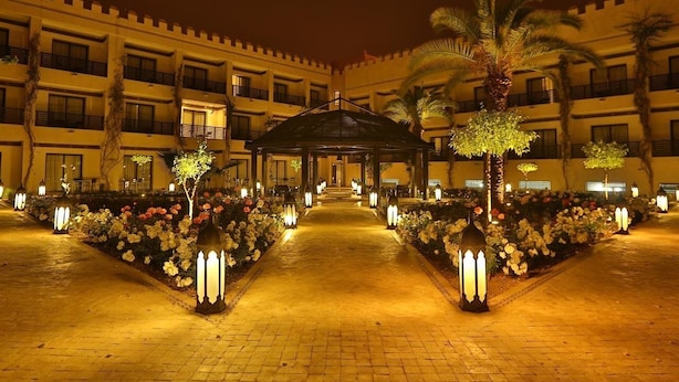 A hotel courtyard at night with a central gazebo, palm trees, and flower beds. - Adam Park Marrakech Hotel & Spa (Marrakech)