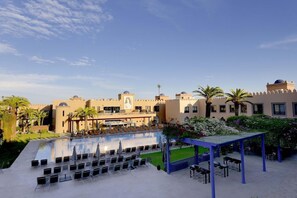 Un espace aménagé au bord de la piscine, avec des chaises longues, un coin salon abrité et un bâtiment doté de structures en forme de dôme.