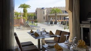A dining area with tables and chairs, a view of the courtyard, and a building with a turret. - Adam Park Marrakech Hotel & Spa (Marrakech)