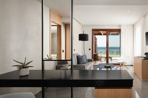 Ett modernt hotellrum med en matplats, en soffa, ett litet bord, en krukväxt och utsikt över havet.