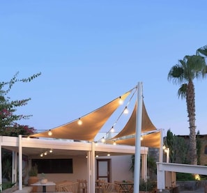 An outdoor patio area with a canopy, tables, chairs, and string lights. - Ikaros Beach Luxury Resort and Spa - Adults Only (Hersonissos)