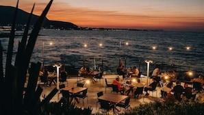 An outdoor dining area with tables and chairs, overlooking a body of water at dusk. - Ikaros Beach Luxury Resort and Spa - Adults Only (Hersonissos)