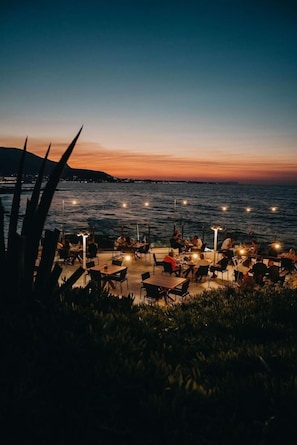 An outdoor dining area with tables and chairs, overlooking a body of water at dusk. - Ikaros Beach Luxury Resort and Spa - Adults Only (Hersonissos)