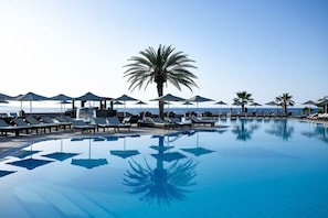 A pool with lounge chairs and umbrellas, palm trees, and a clear view of the sea. - Ikaros Beach Luxury Resort and Spa - Adults Only (Hersonissos)