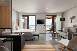 A modern hotel room with a bed, a desk, a sofa, and a TV. There are large windows with a view of the sea. - Ikaros Beach Luxury Resort and Spa - Adults Only (Hersonissos)