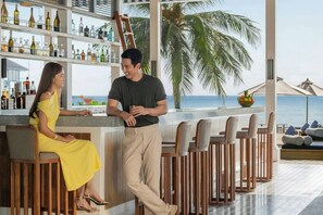 A bar area with a view of the ocean, a bar counter, and a seating area with wooden chairs. - The Halcyon Private Isles Maldives (Meradhoo)