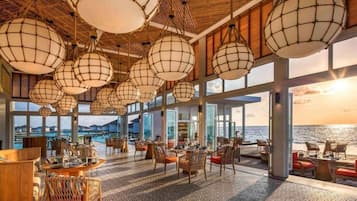 Un espacio interior amplio con ventanas grandes, muebles de mimbre e iluminación colgante esférica.