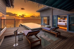 A wooden deck with lounge chairs, a hot tub, and a glass-enclosed bedroom with a view of the sunset over the ocean. - The Halcyon Private Isles Maldives (Meradhoo)