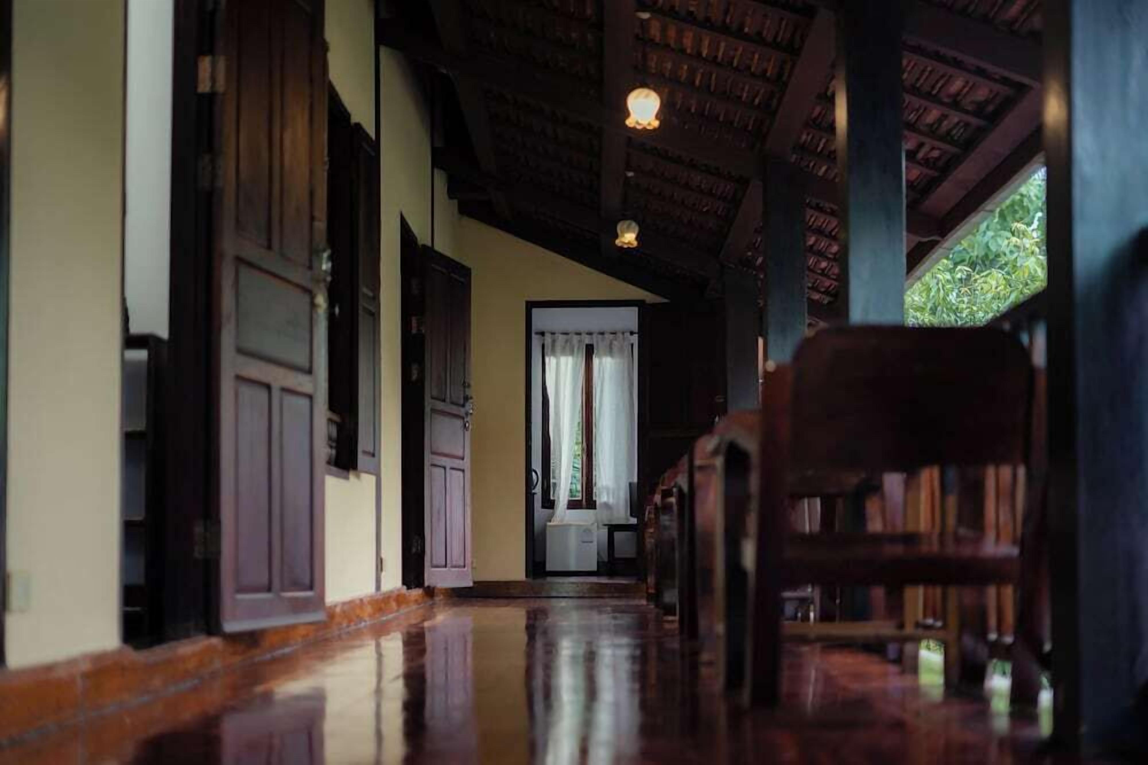 A corridor with wooden floors, a wooden door, and a window with curtains.