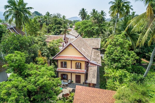 A two-story house with a tiled roof, surrounded by lush greenery and palm trees. - Khoum Xieng Thong Boutique Villa (Luang Prabang)