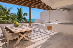 Un patio moderno al aire libre con una mesa de comedor, sillas de mimbre, una pequeña área de cocina y vistas al océano.