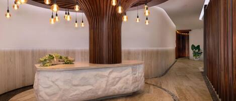 A reception area with a central wooden column, a stone bench, and hanging light fixtures.