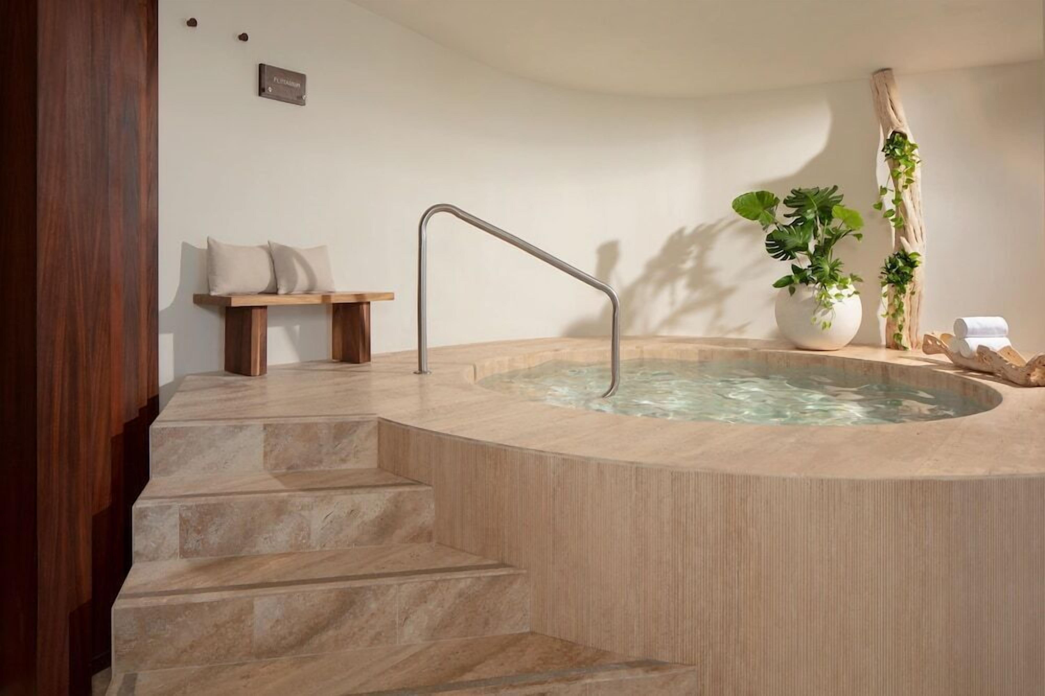 A spa area with a hot tub, wooden steps, a bench, and potted plants.