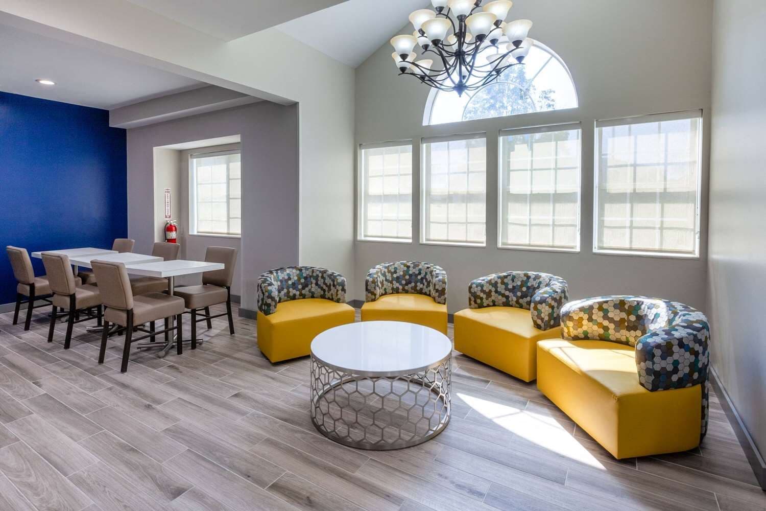 Un intérieur moderne avec un coin repas, des canapés jaunes et une grande fenêtre laissant entrer la lumière naturelle.