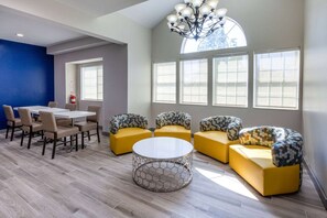 A modern interior with a dining area, yellow sofas, and a large window providing natural light. - Microtel Inn & Suites by Wyndham Sunbury/columbus North (Sunbury)