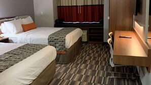 A hotel room with two beds, a desk, a chair, a TV, and a window with curtains.