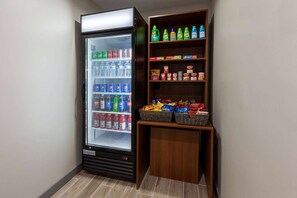 A corner with a beverage refrigerator stocked with various drinks and a shelf with snacks and beverages. - Microtel Inn & Suites by Wyndham Sunbury/columbus North (Sunbury)