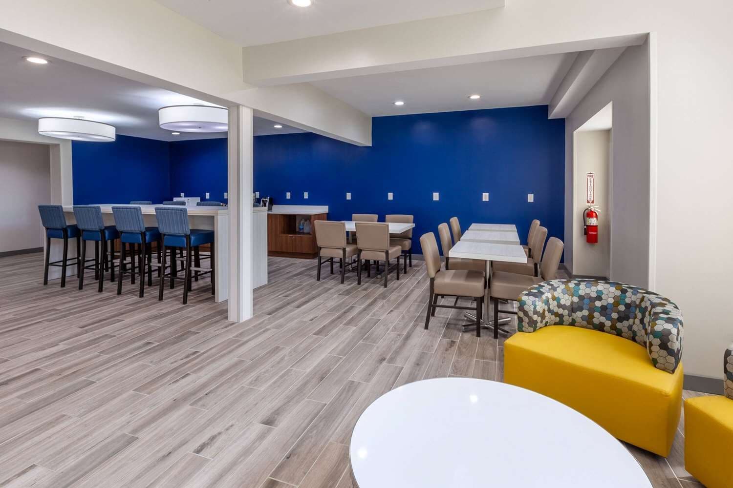 A modern dining area with high tables and chairs, a central bar, and a yellow sofa.