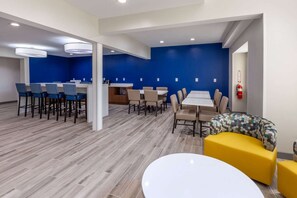 A modern dining area with high tables and chairs, a central bar, and a yellow sofa. - Microtel Inn & Suites by Wyndham Sunbury/columbus North (Sunbury)