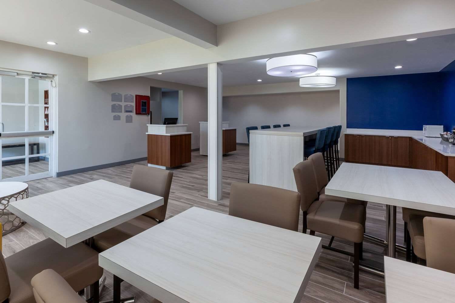 Un hall d’hôtel moderne avec un comptoir d’accueil, un espace salon et, au fond, une vue sur la cuisine.