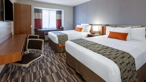 A hotel room with two beds, a desk with a chair, a TV, and a window with curtains.
