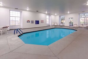 Una piscina cubierta con señalización clara de las normas, una silla de socorrista y una escalera de piscina.