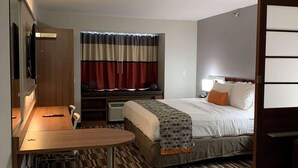 A hotel room with a bed, a desk, a chair, a TV, and a window with curtains.