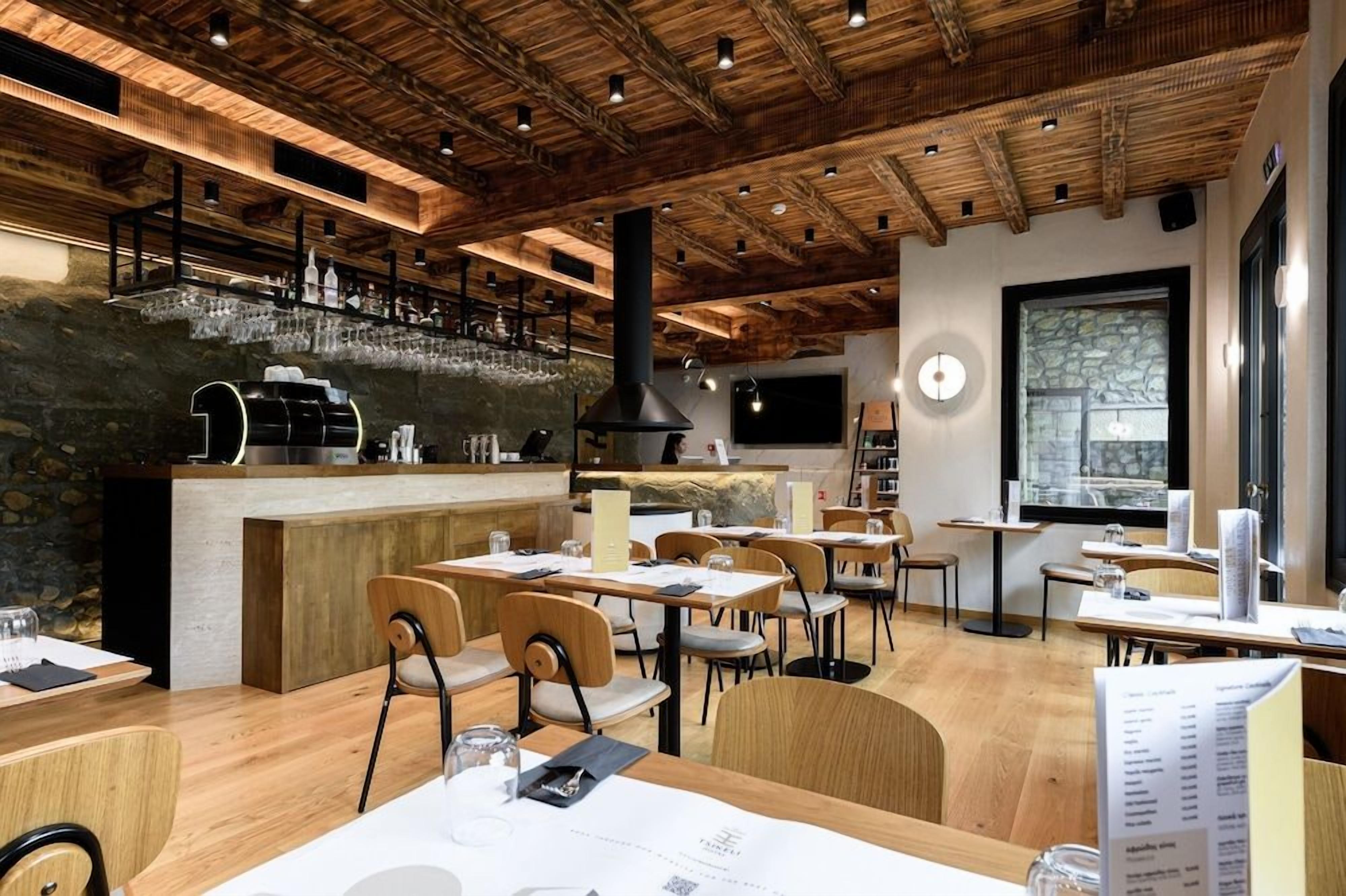 Un restaurante con vigas de madera en el techo, una zona de bar con vasos y mesas con menús.