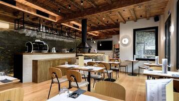 Un restaurante con vigas de madera en el techo, una zona de bar con vasos y mesas con menús.