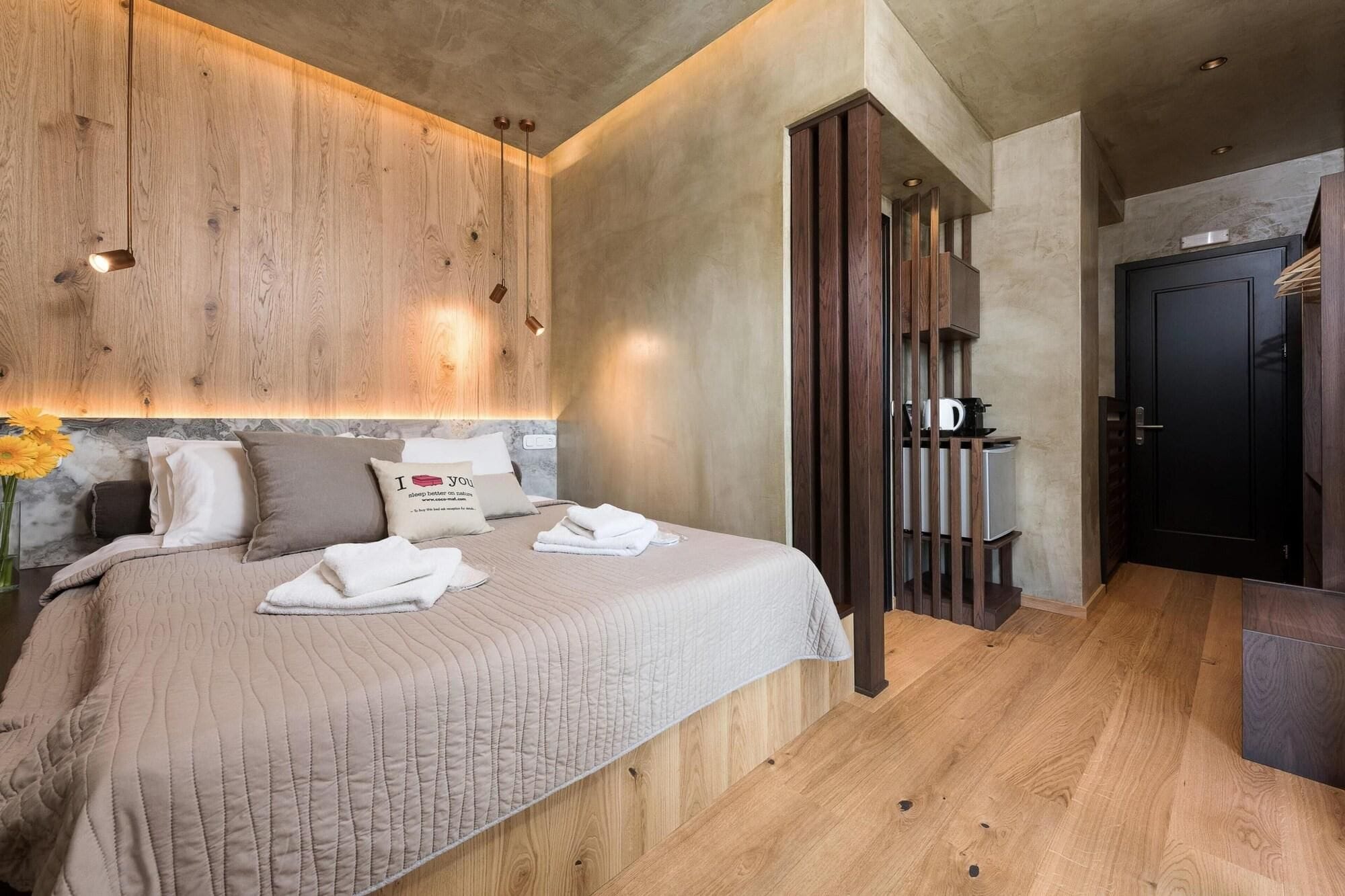 Ein Hotelzimmer mit einem großen Bett, einem Holzkopfteil, einer kleinen Küchenzeile und einer dunklen Tür.