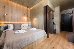 A hotel room with a large bed, wooden headboard, a small kitchenette, and a dark door. - Tsikeli Boutique Hotel Meteora (Kalabaka)
