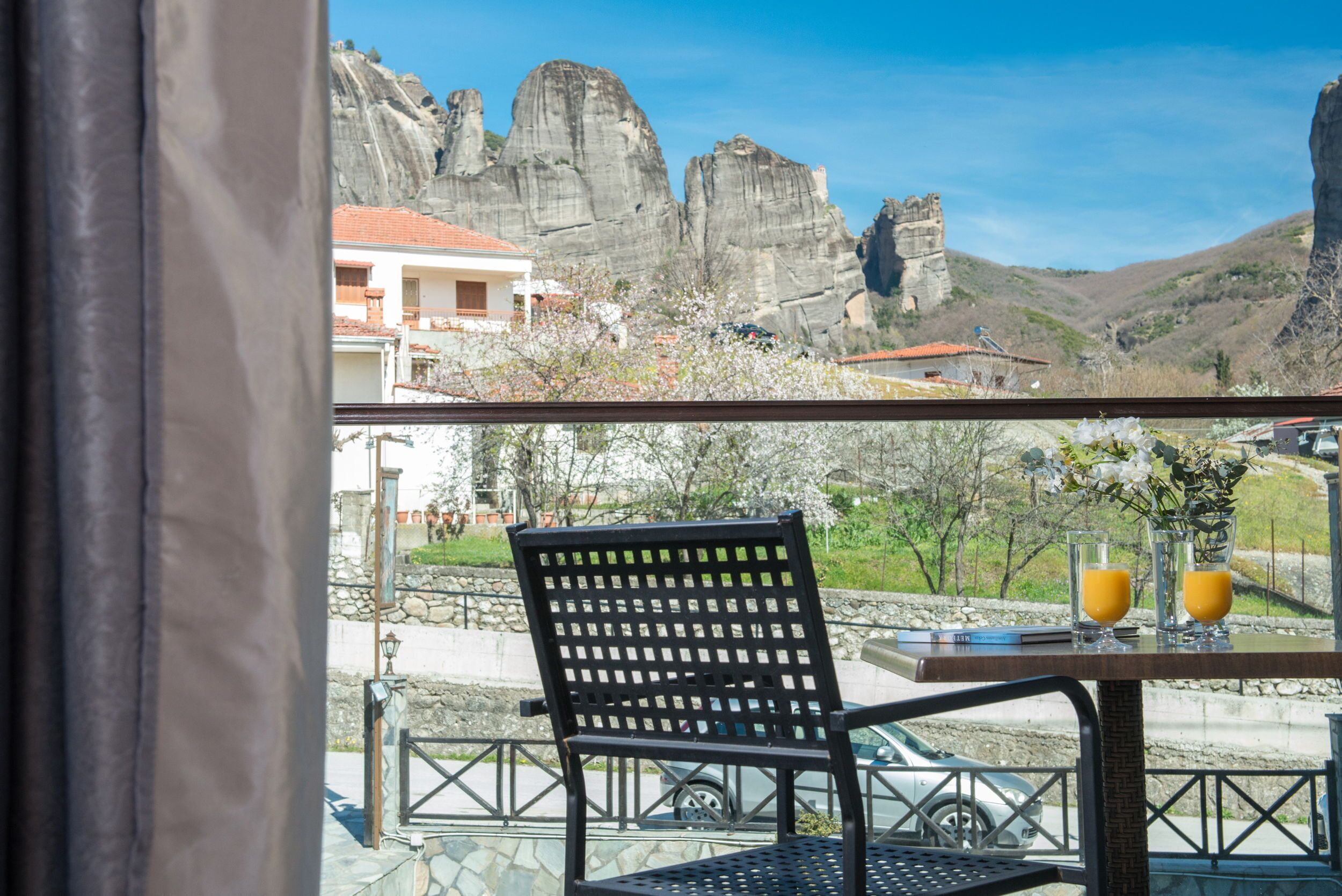 Una mesa con dos vasos de jugo de naranja, una silla y vistas a formaciones rocosas y un edificio.