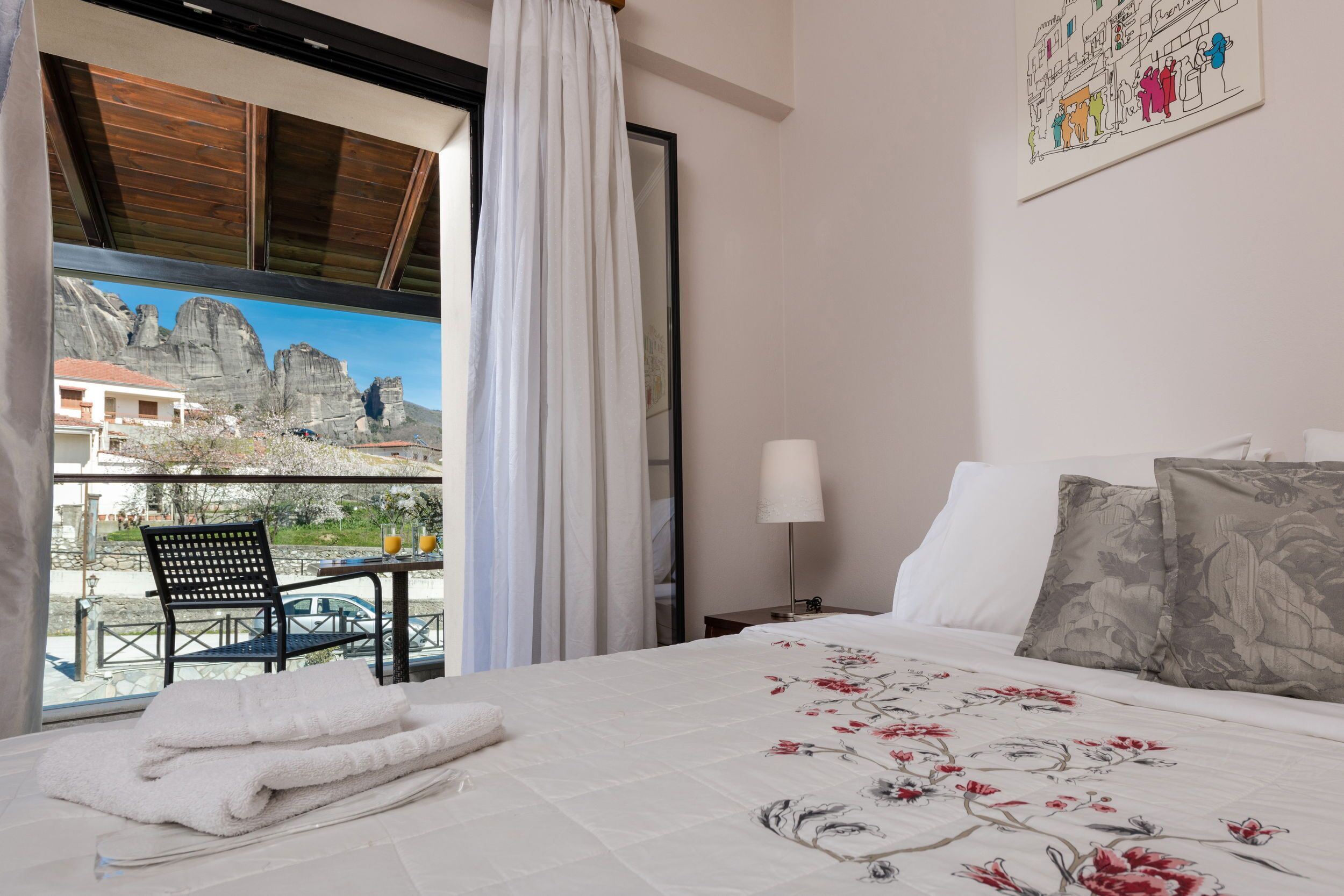 Habitación de hotel con cama, mesita de noche, lámpara, una silla y vistas a montañas a través de una ventana.