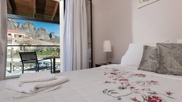 Habitación de hotel con cama, mesita de noche, lámpara, una silla y vistas a montañas a través de una ventana.