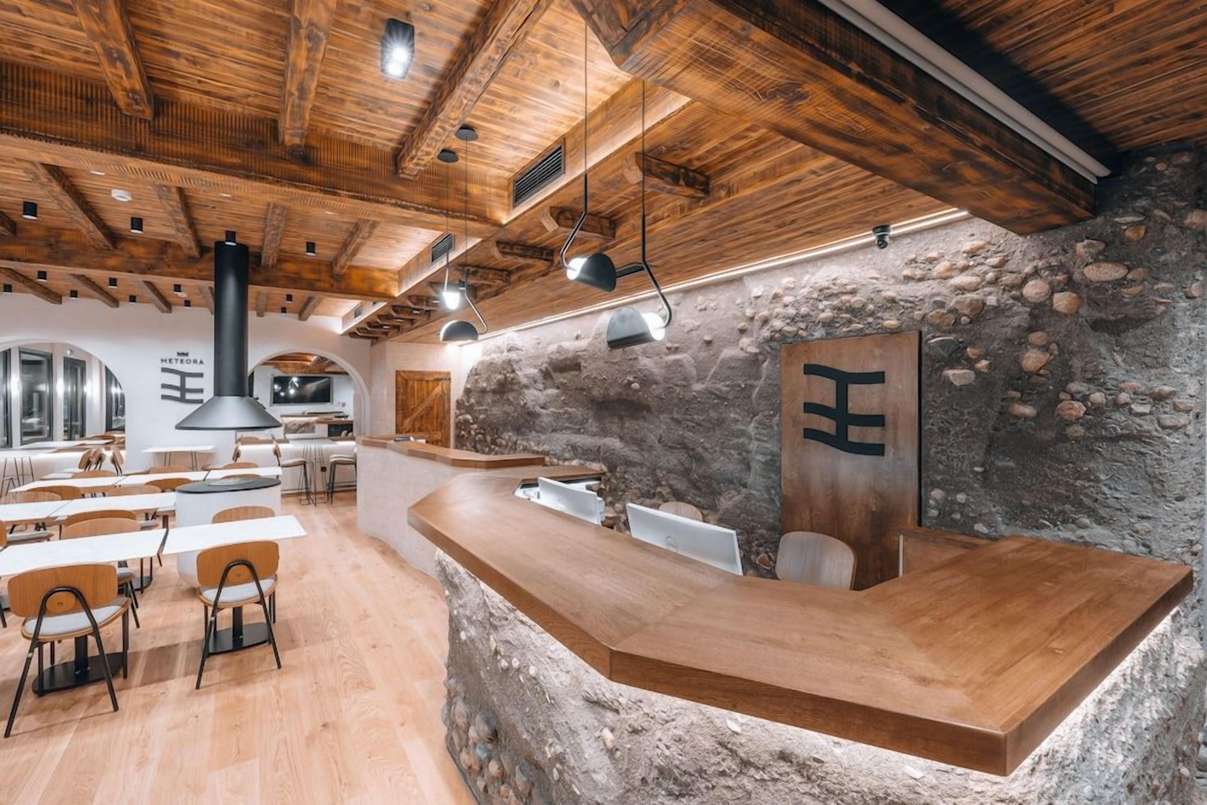 Interior de un restaurante con vigas de madera en el techo, paredes de piedra y una larga barra con asientos.
