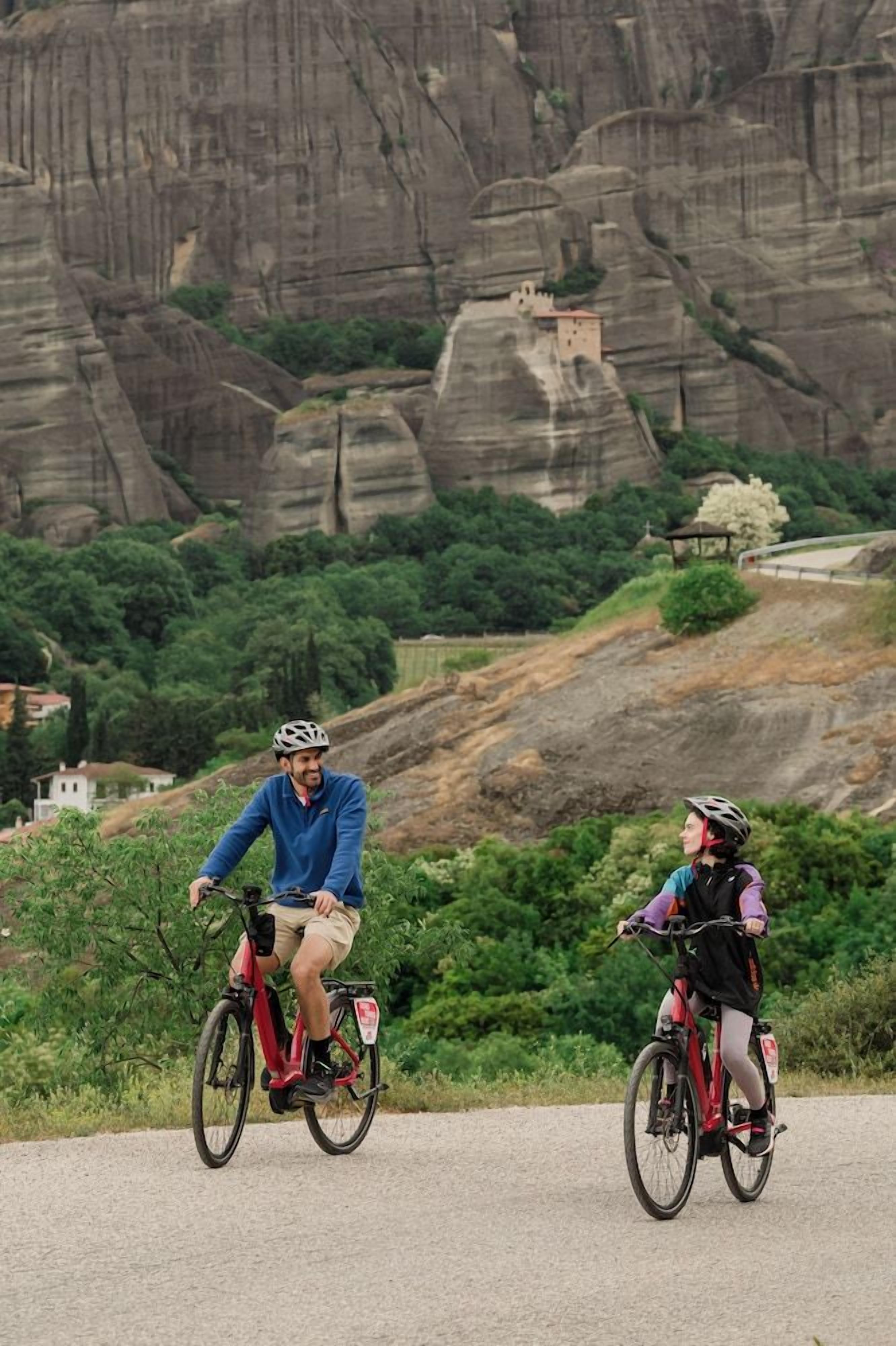 Dos ciclistas en un sendero de grava con montañas al fondo.