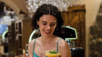 Una persona sentada en la barra sosteniendo una bebida, rodeada de copas colgantes.